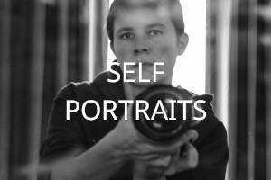 . A black and white self portrait of me (a white woman with short dark hair) holding a camera over my torso. Over the image the words 'Self Portraits' are written in uppercase white letters.