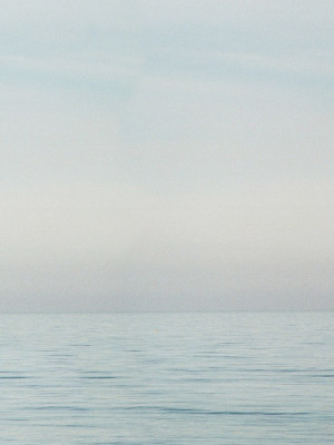 A soft colour photograph of the seaside. The top two third contains a featureless sky, the bottom third contains the sea and gentle ripples on its surface.