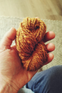 A vertical colour photograph of a small caramel coloured skein of wool held in my white hand. The thickness is not regular throughout.