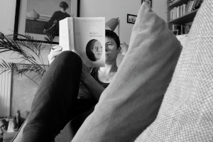 A horizontal black and white photograph of me (a white woman with short black hair and dark trousers) reclining on the sofa, reading the book 'Seeing Ourselves: Women's Self-Portraits' by Frances Borzello.